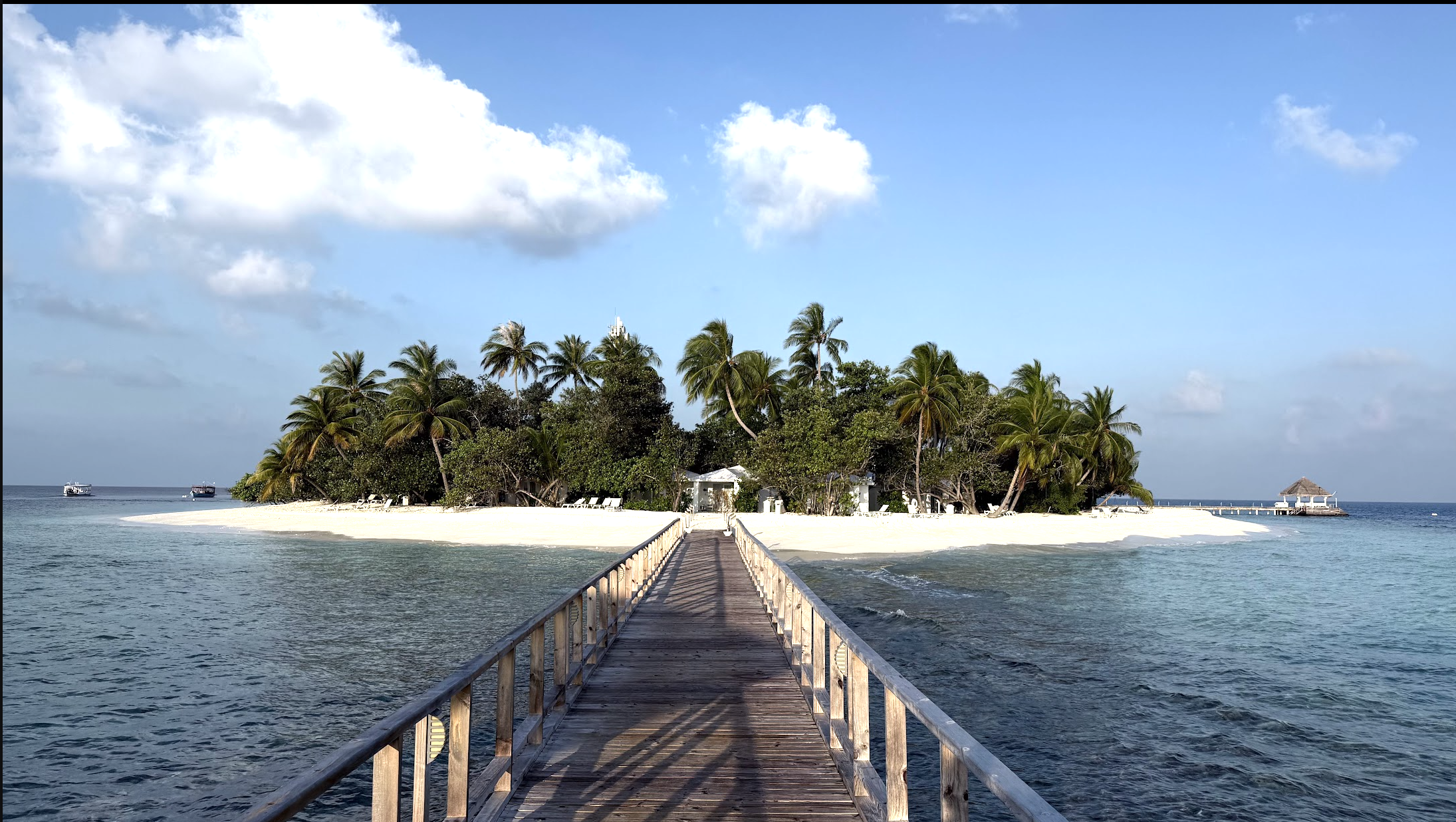 A wooden pier leading to a secluded tropical island with lush greenery and white sand.
