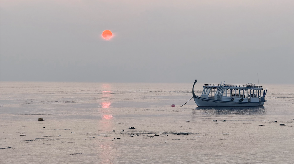 A calm Maldives morning with a soft sunrise, highlighting a boat on tranquil waters.
